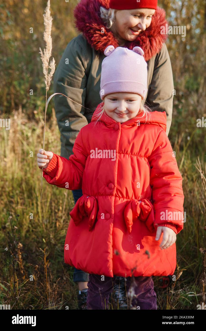 A little girl in a red coat walks in nature in an autumn grove with her ...