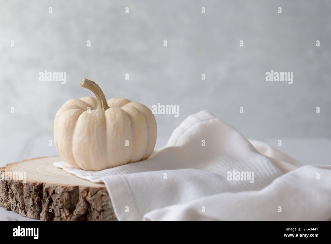 Baby Boo Ghost pumpkin on wooden block with cream linen napkin against a light background. Crisp, light and airy still life . with space for copy Stock Photo