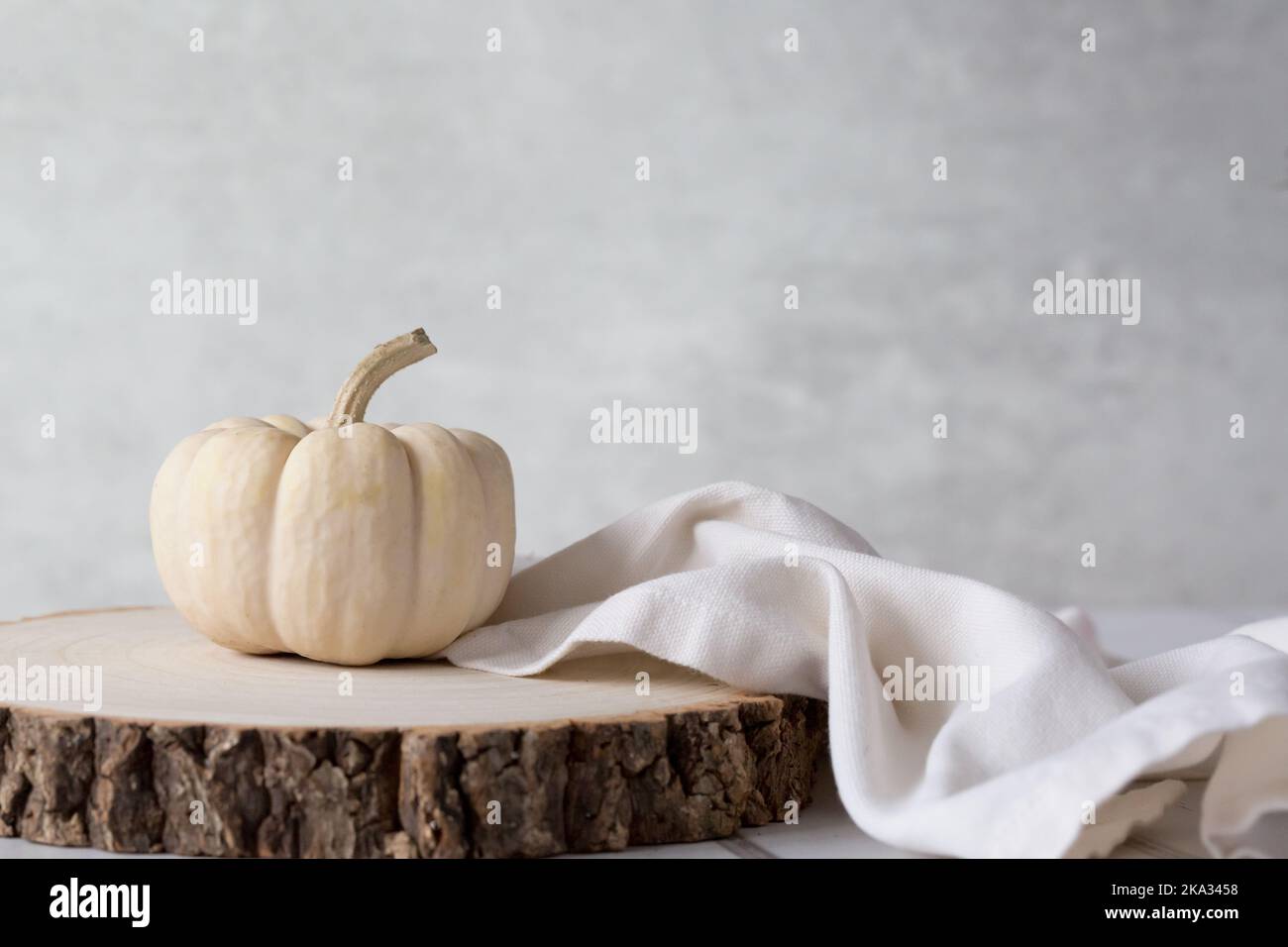 Baby Boo Ghost pumpkin on wooden block with cream linen napkin against a light background. Crisp, light and airy still life. Space for copy Stock Photo