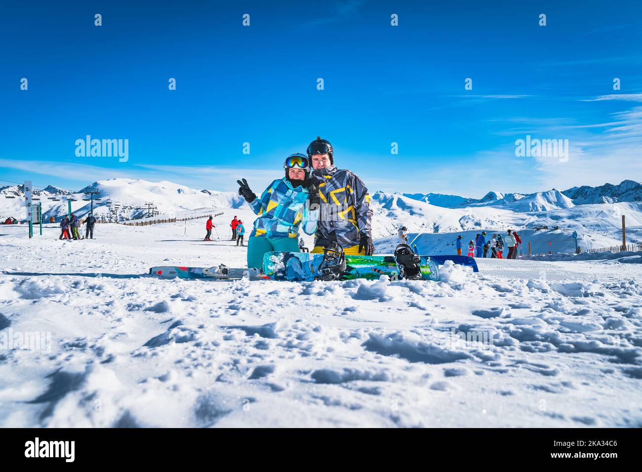 Couple, skier and snowboarder sitting on the snow and looking at camera, Pyrenees Mountains. Winter ski holidays in El Tarter, Grandvalira Andorra Stock Photo