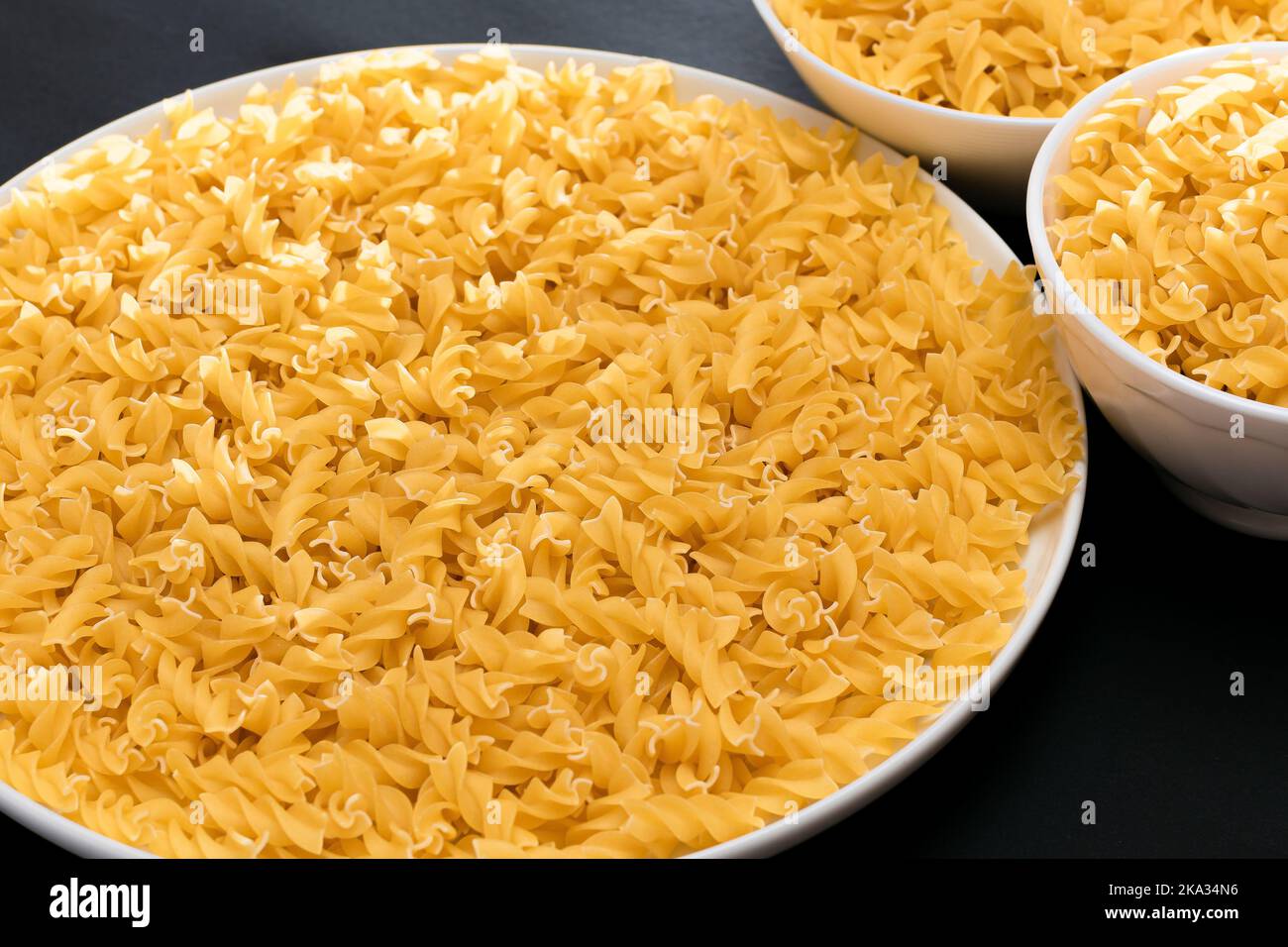 Uncooked Fusilli Pasta Lying on White Plate on Black Background. Raw