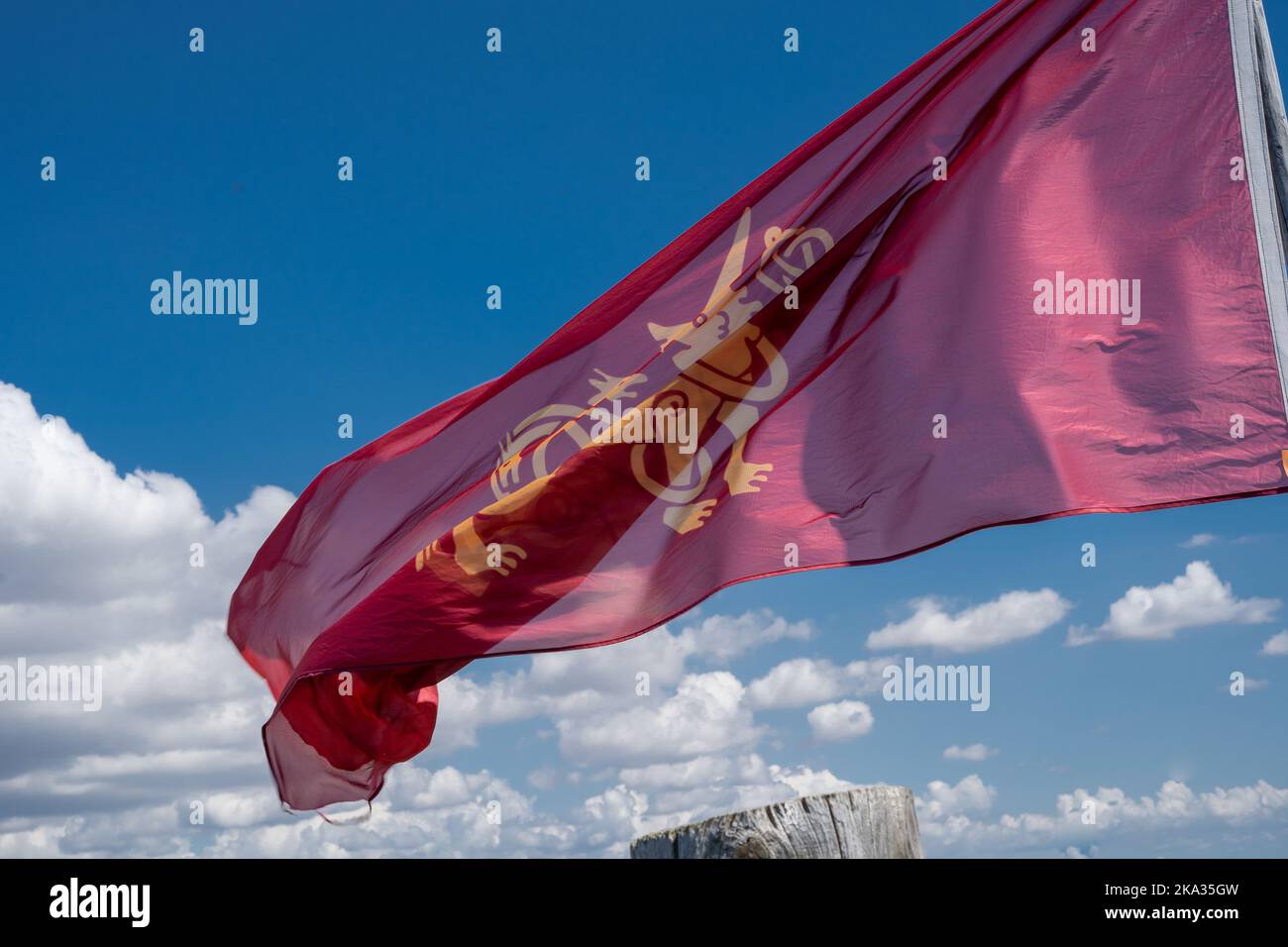 A red flag with the image of a lion develops under a blue cloudy sky ...