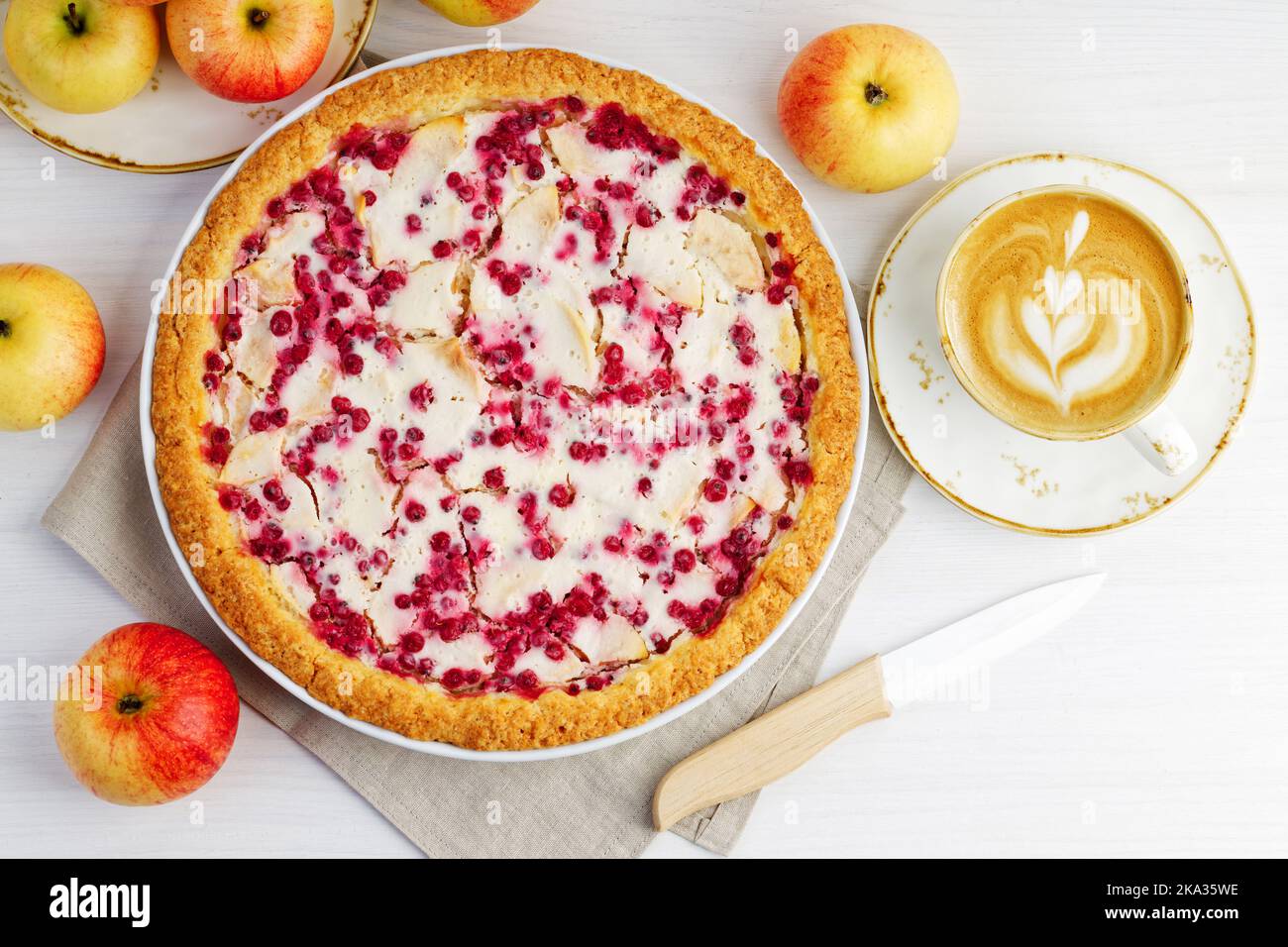 Homemade apple and redcurrant pie and cup of coffee cappuccino on white wooden table. Top view. Stock Photo