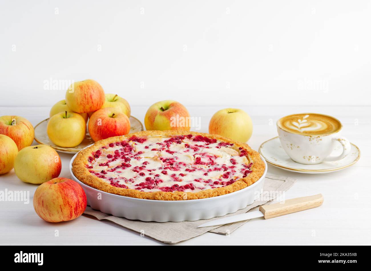Homemade apple and redcurrant pie and cup of coffee cappuccino on white wooden table. Copyspace. Stock Photo