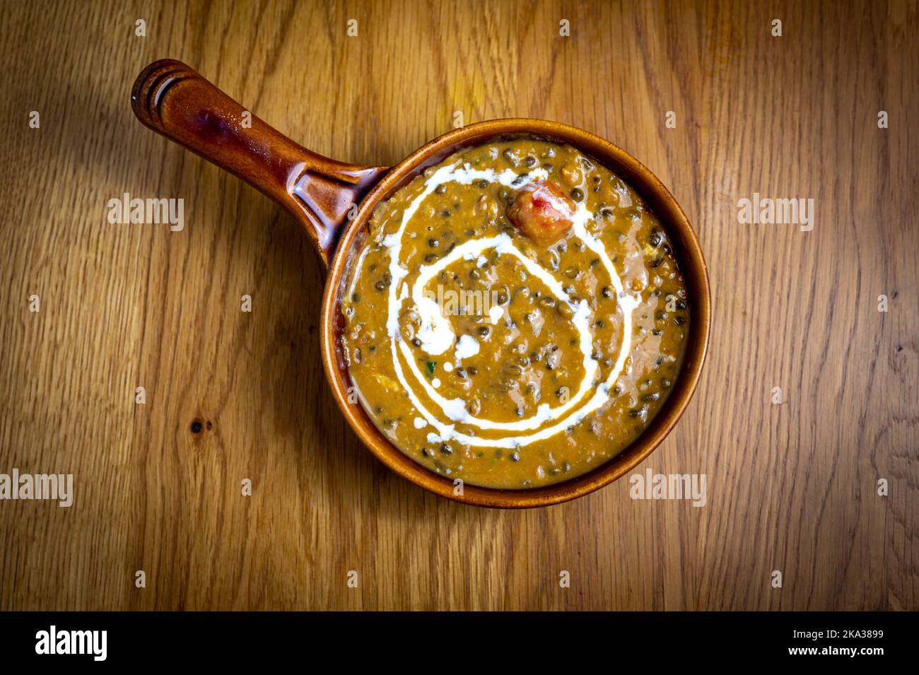 An earthenware bowl containing black  lentil dahl curry on a table in an indian restaurant. Stock Photo