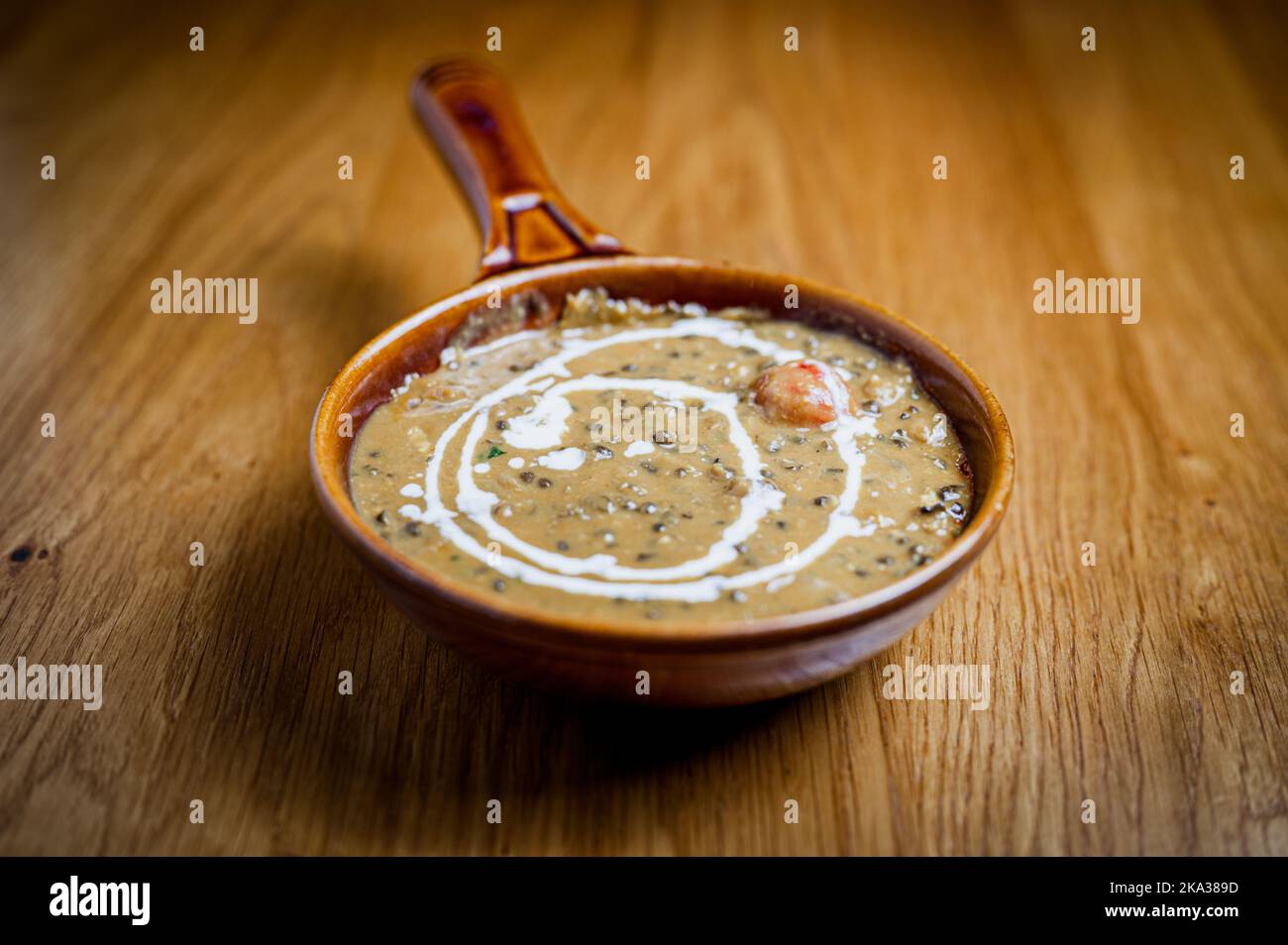An earthenware bowl containing black  lentil dahl curry on a table in an indian restaurant. Stock Photo
