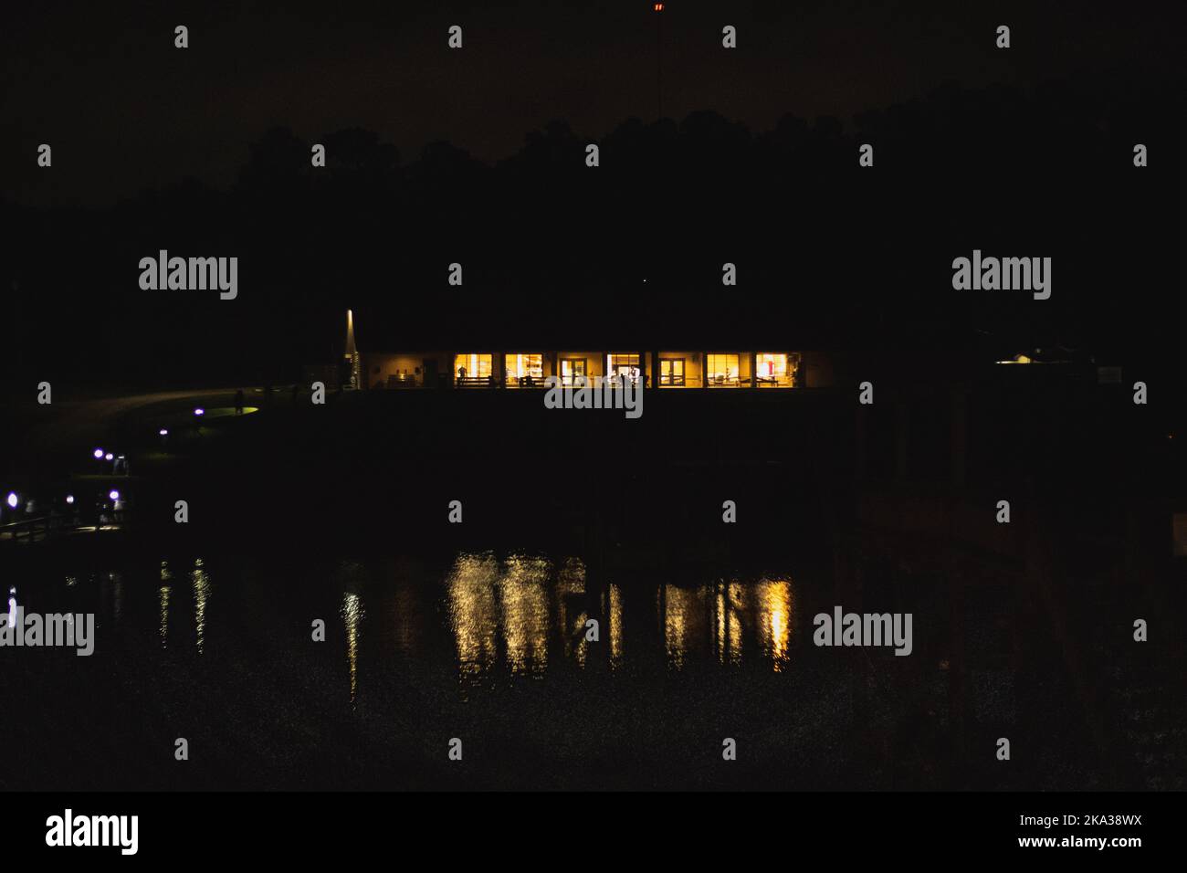 The bright yellow lights lightning the building seen over the lake on a dark evening Stock Photo