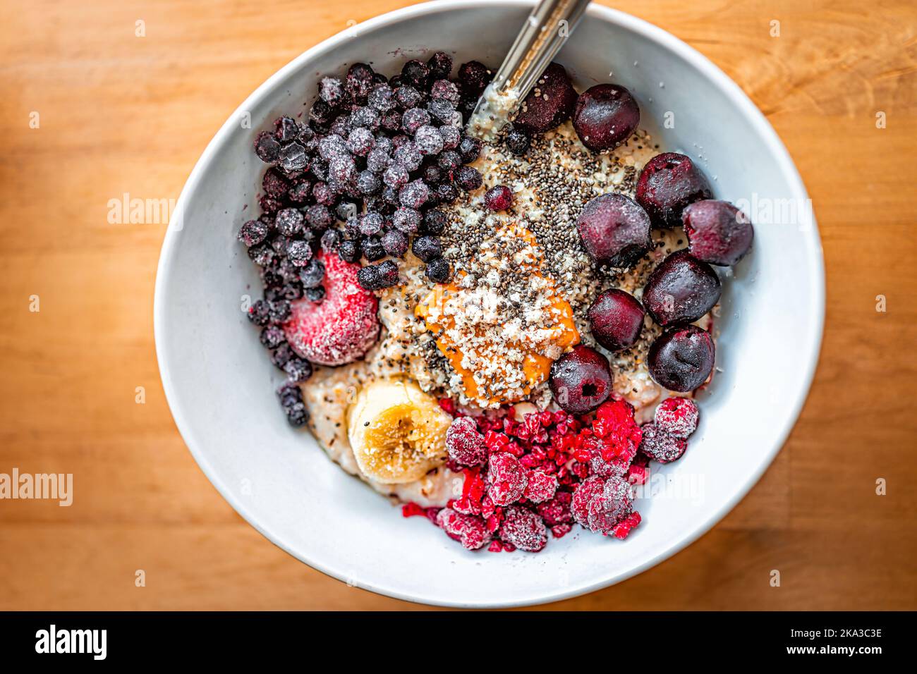 Flat top above looking down on breakfast oatmeal oat porridge bowl with peanut butter, frozen berries raspberries blueberries and cherries with banana Stock Photo