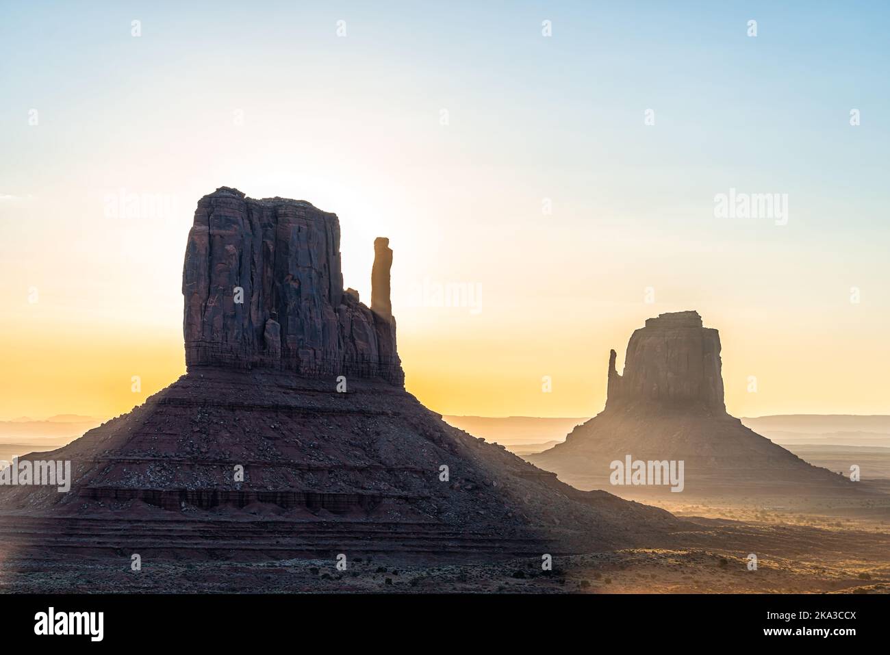 Closeup of east and west mitten buttes and horizon in Monument Valley at sunrise colorful light and sun beam rays behind rock formations in Arizona Stock Photo