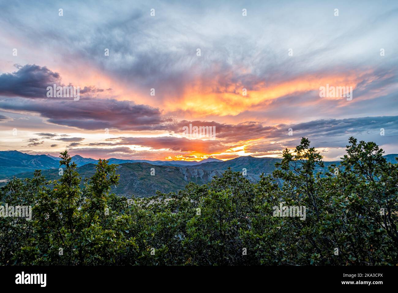 Aspen, Colorado Rocky mountains colorful sunset orange yellow light in sky wide angle view of blue skyscape, storm clouds foreground of oak trees Stock Photo
