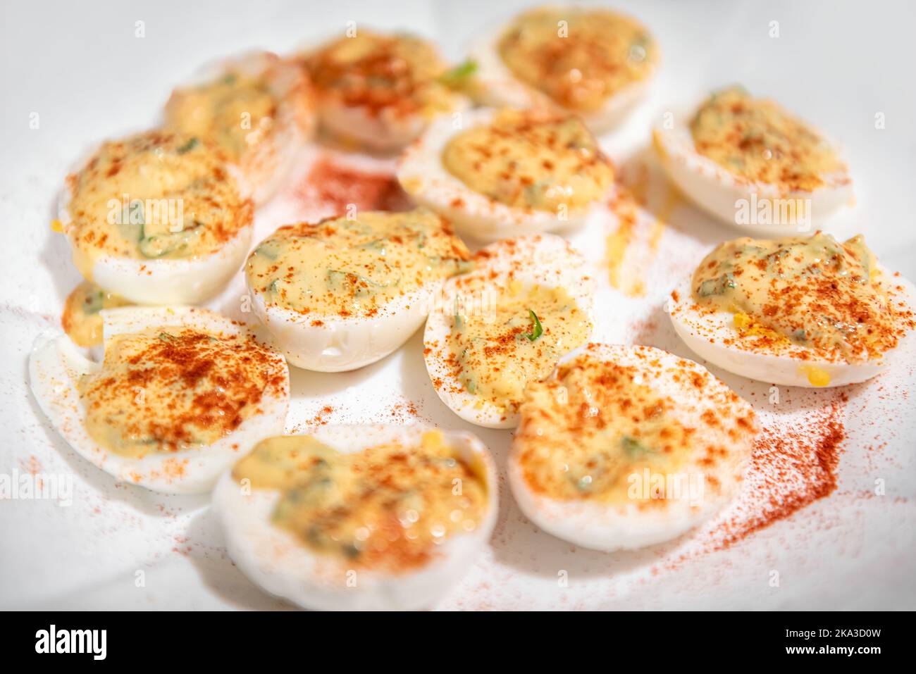 Macro closeup of deviled eggs hard boiled on white plate with mayonnaise, paprika seasoning and parsley Stock Photo