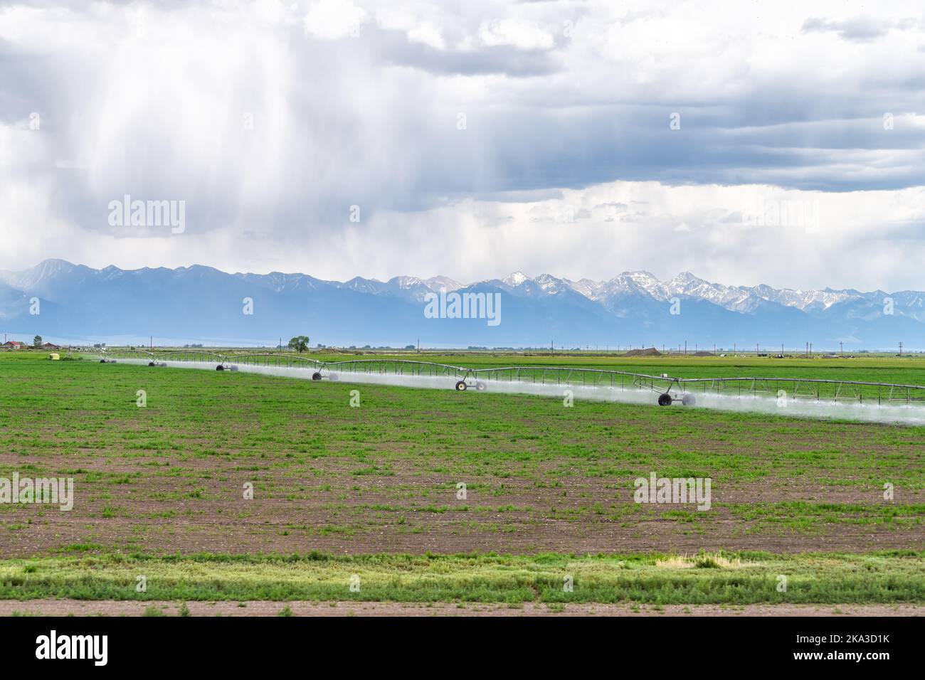 Highway 285 in Colorado with rural countryside farms near Monte Vista and view of Rocky Mountains with water sprayer irrigation sprinkler farming equi Stock Photo