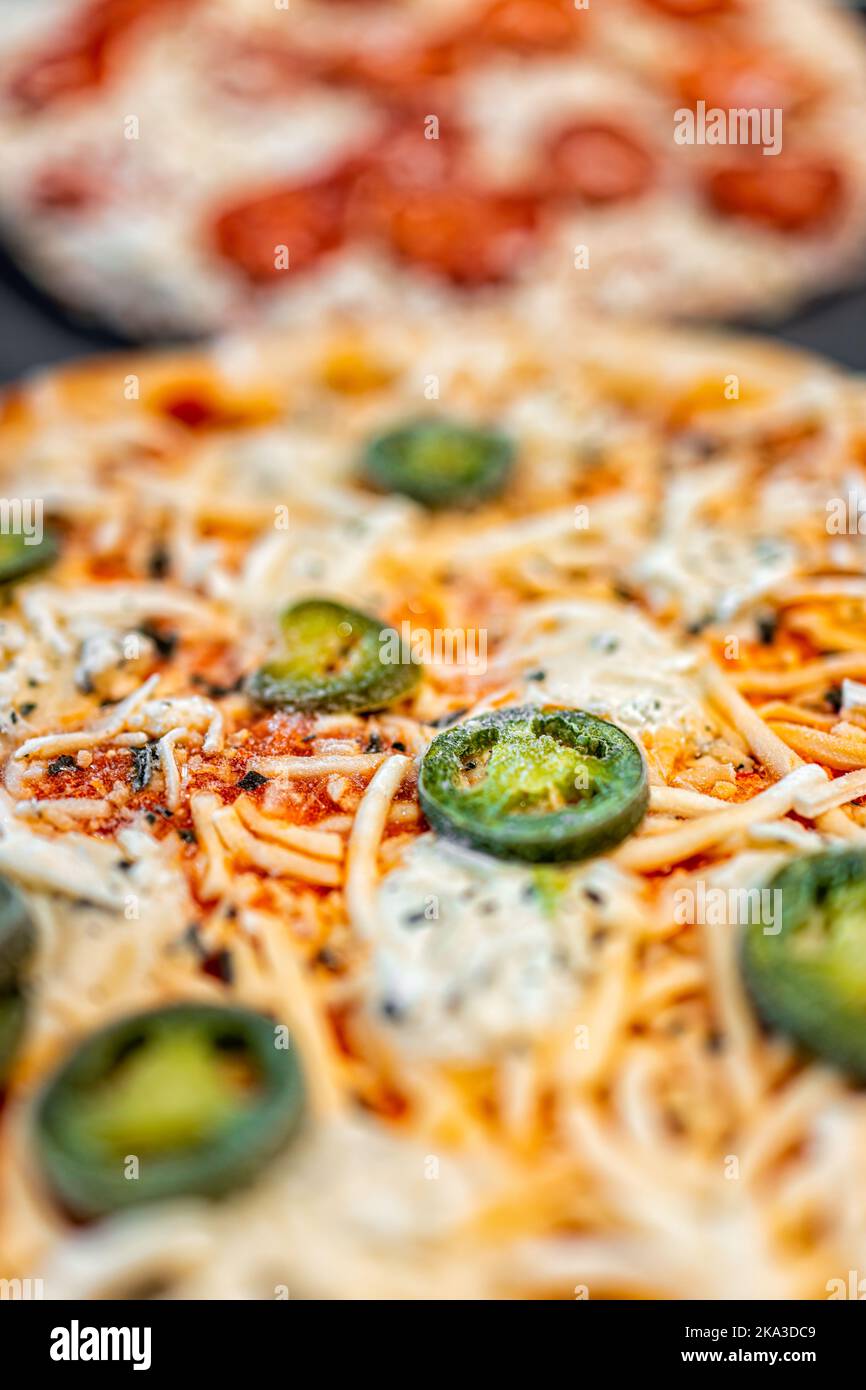 Macro closeup vertical view of uncooked raw take and bake frozen pepperoni shredded mozzarella cheese and jalapeno pizza pie on tray ready for baking Stock Photo