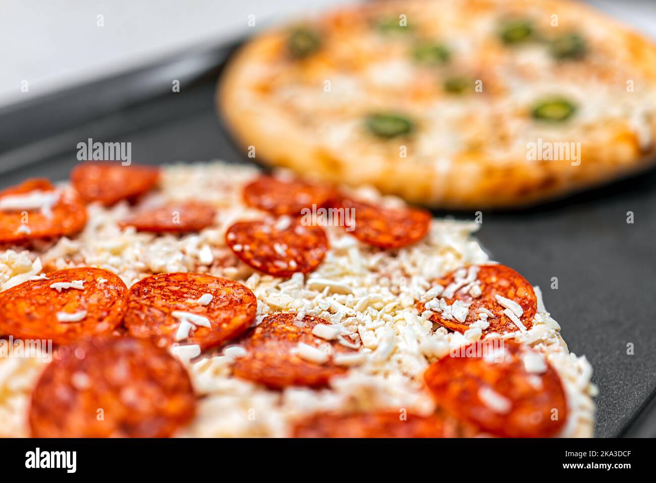 Macro closeup of uncooked raw take and bake frozen pepperoni shredded mozzarella cheese and jalapeno pizza pie on tray ready for baking cooking on kit Stock Photo