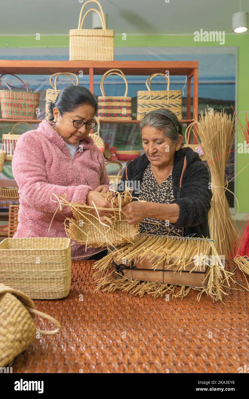 Hispanic mother and daughter weaving baskets from dry grass while