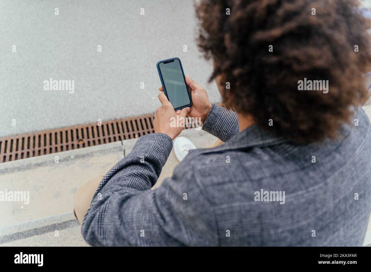 From above African American male tourist in casual clothes sitting on steps and browsing smartphone Stock Photo