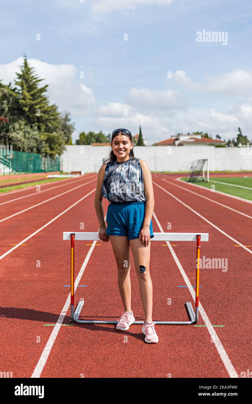 Full body glad young ethnic female athlete in sportswear standing near