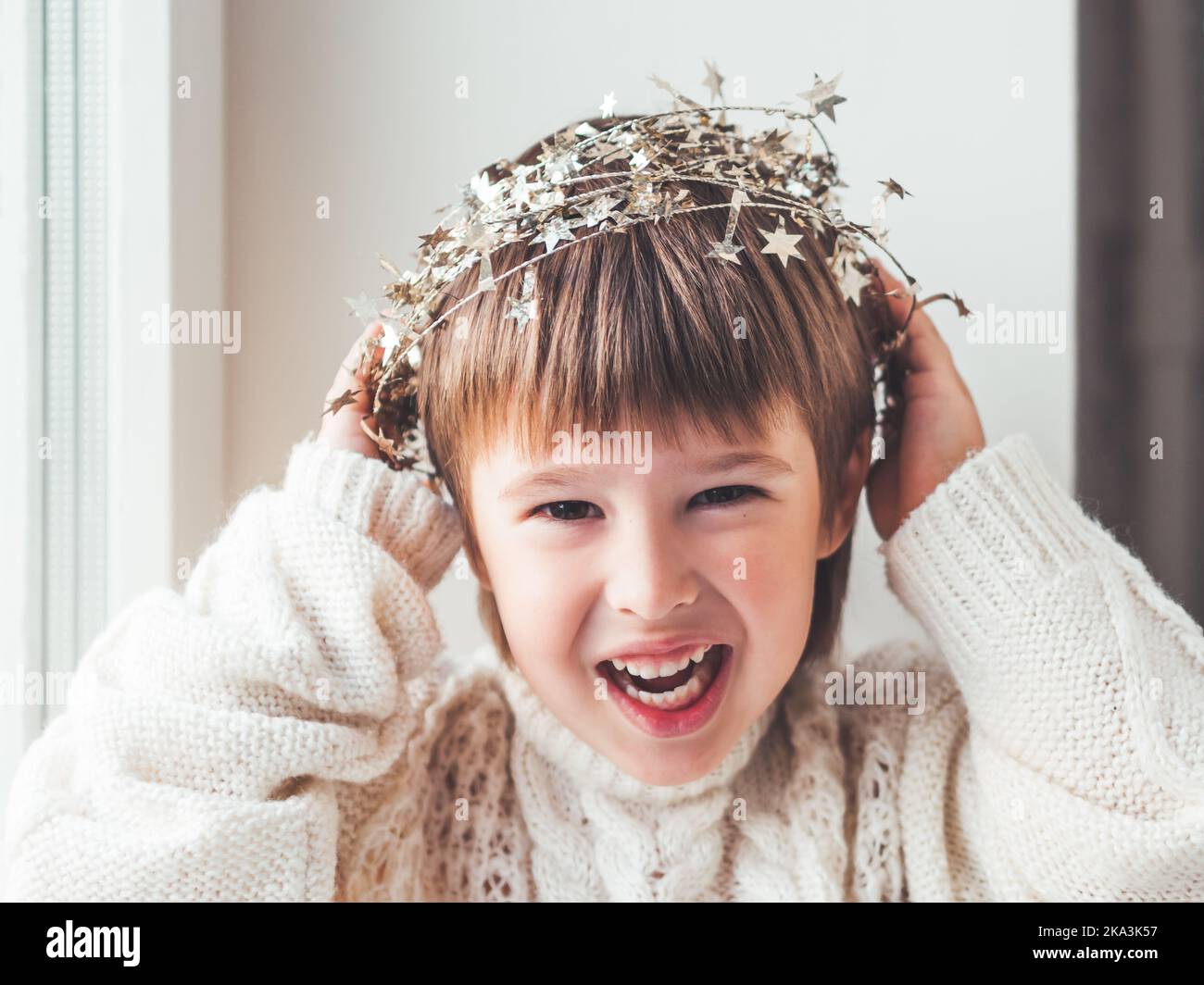 Kid with decorative star tinsel for Christmas tree. Boy in cable-knit oversized sweater. Cozy outfit for snuggle weather. Winter holiday spirit. Stock Photo