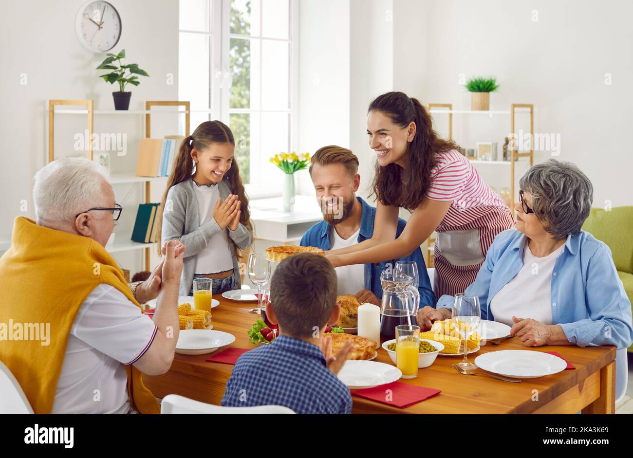 Big family has a lunch sitting at table enjoys the pie in mom's hands in loving room at home. Stock Photo