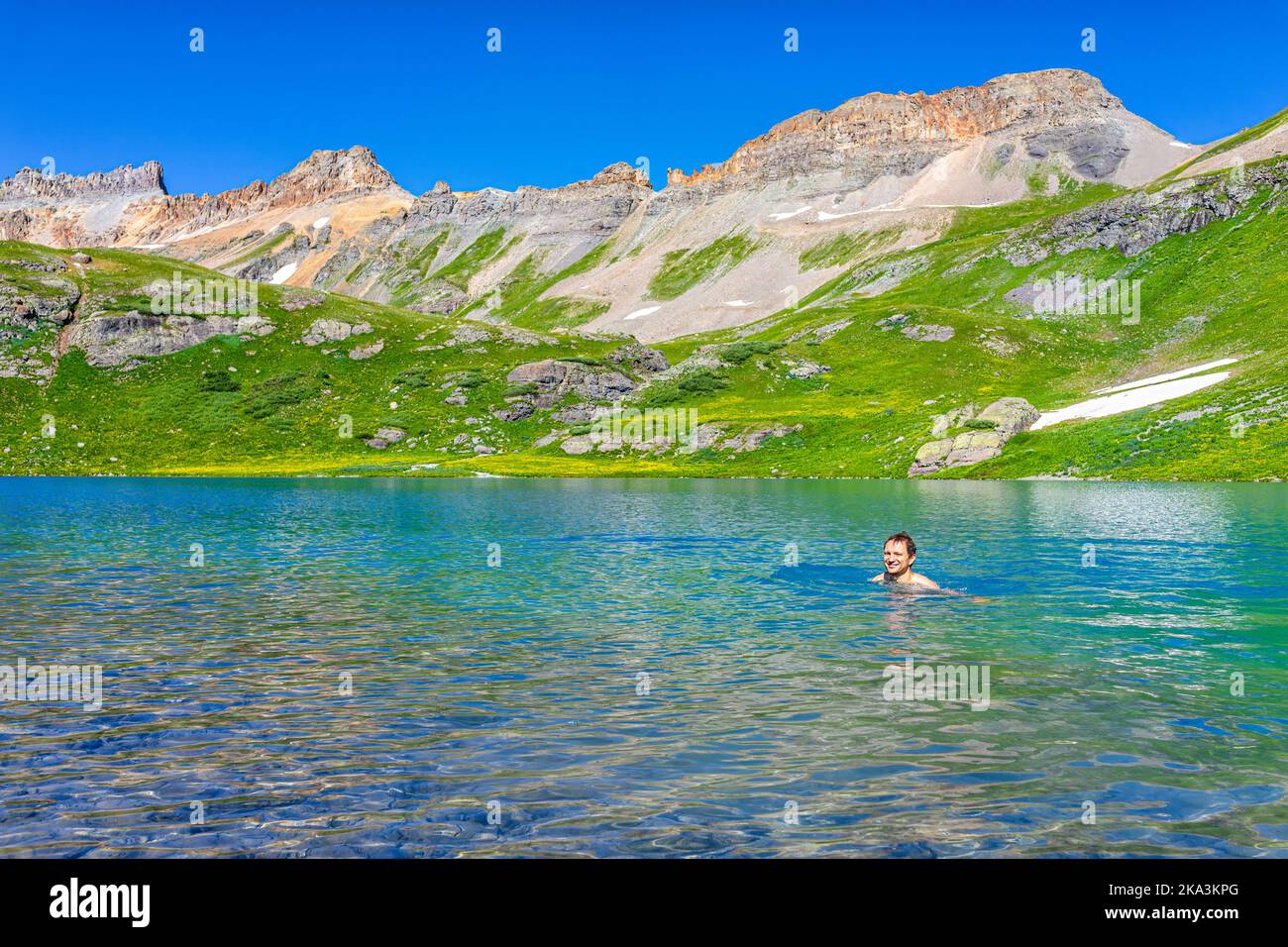 One young happy man swimming in colorful turquoise water of Ice Lake on hiking trail in Silverton, Colorado in San Juan Mountains in summer Stock Photo