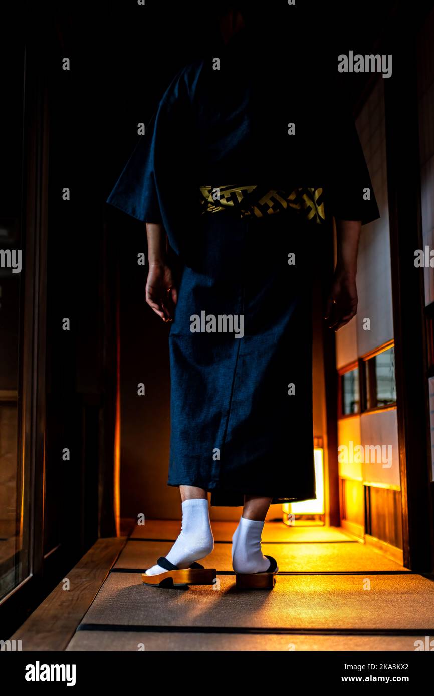 Unrecognizable man in Japanese kimono walking with geta socks and tabi shoes by shoji sliding paper doors at night and tatami mat vertical view in tra Stock Photo