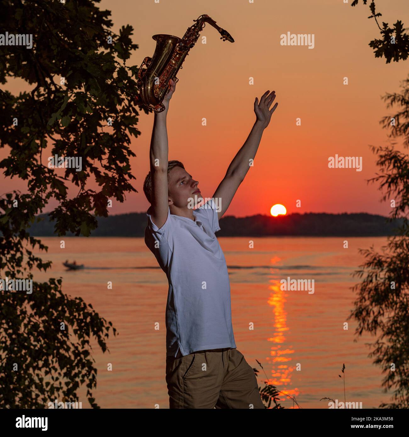 A young man with a saxophone raised his hands up, enjoying the sunset. Stock Photo