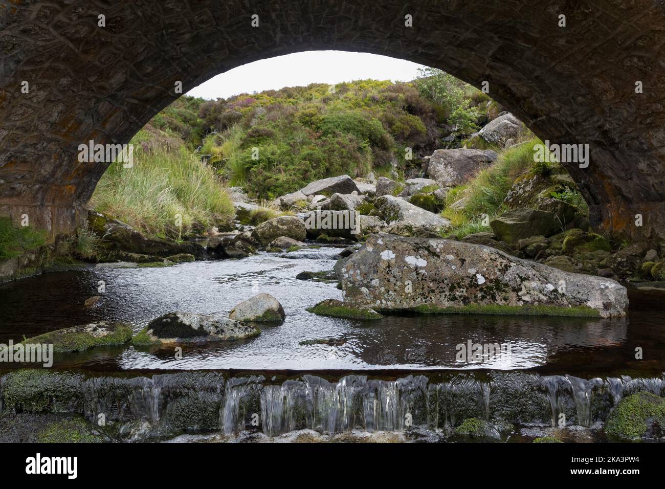 A Rocky River With Cascades Under An Arch Bridge In Glendalough a-rocky-river-with-cascades-under-an-arch-bridge-in-glendalough