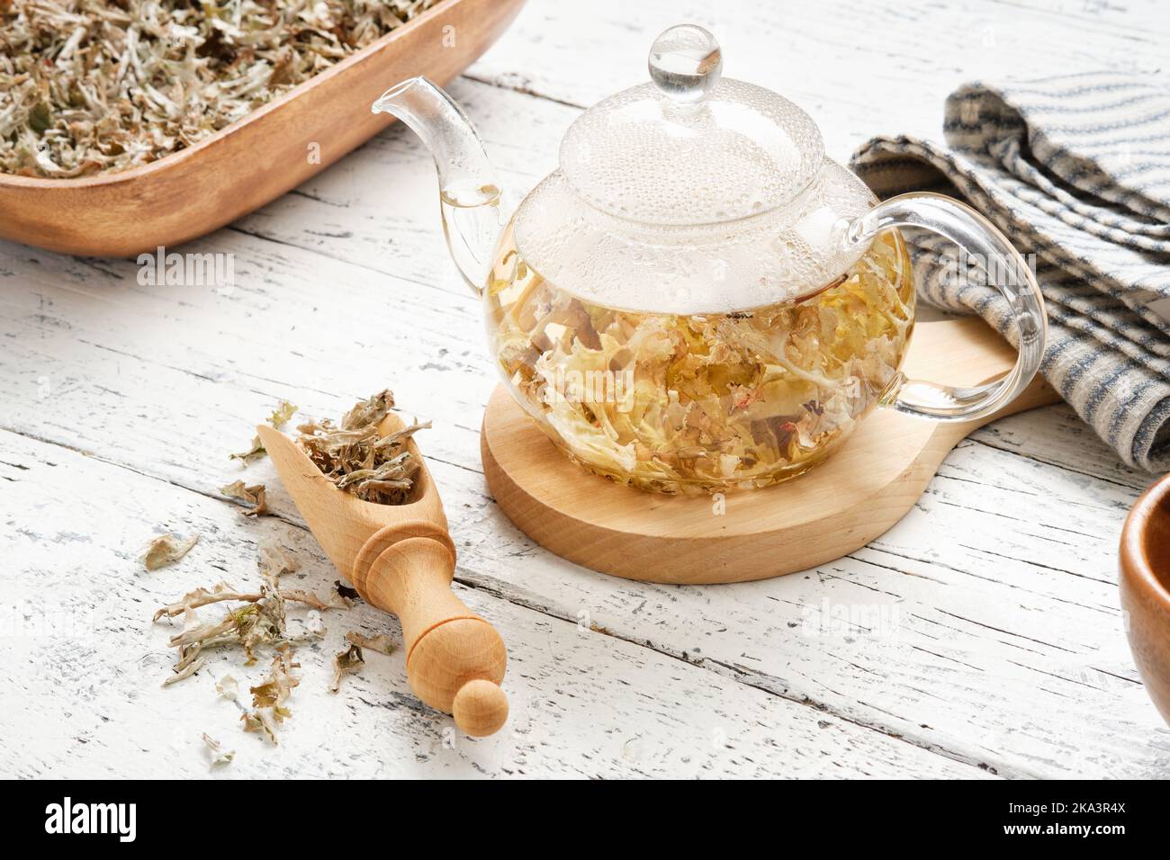 Glass tea kettle of herbal Icelandic moss tea. Wooden scoop and bowl of dried Iceland moss. Cetraria islandica - latin name of plant. Alternative herb Stock Photo