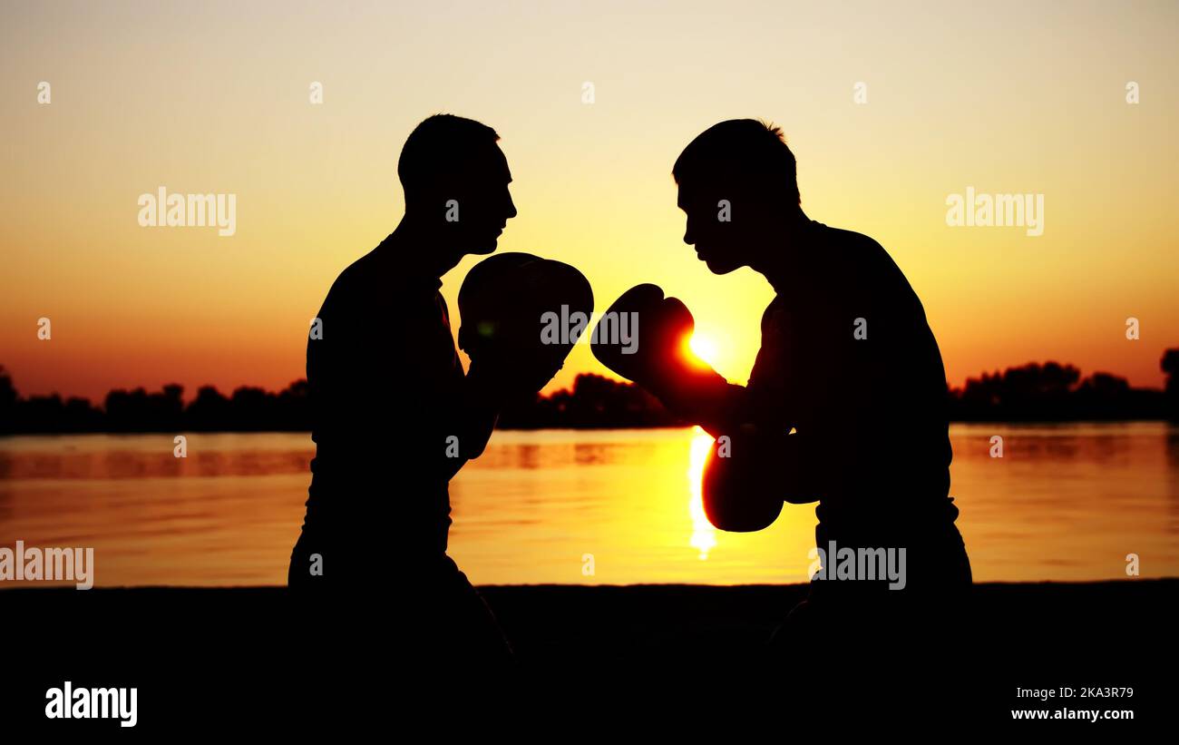 Two dark male figures, at sunrise, against the light, boxing, fighting