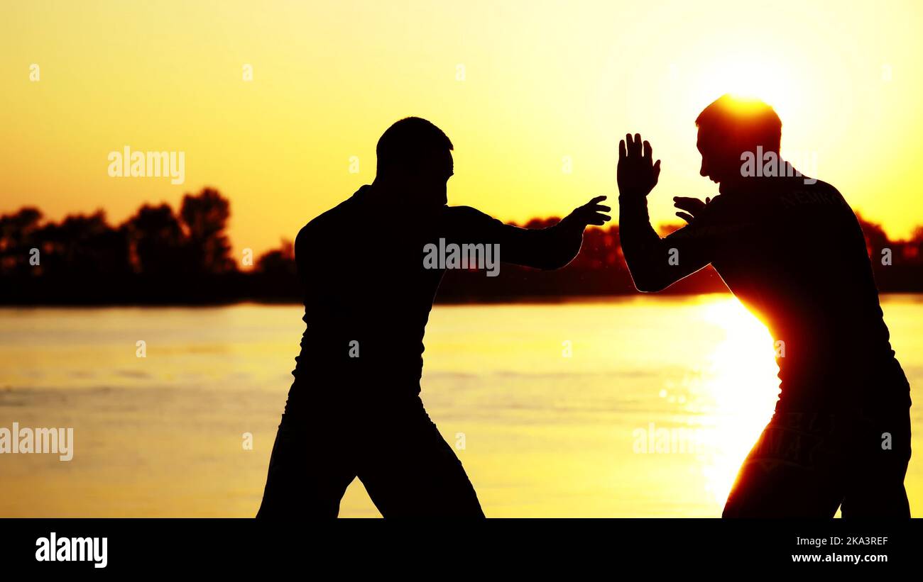 Two dark male figures, at sunrise, against the light, boxing, fighting