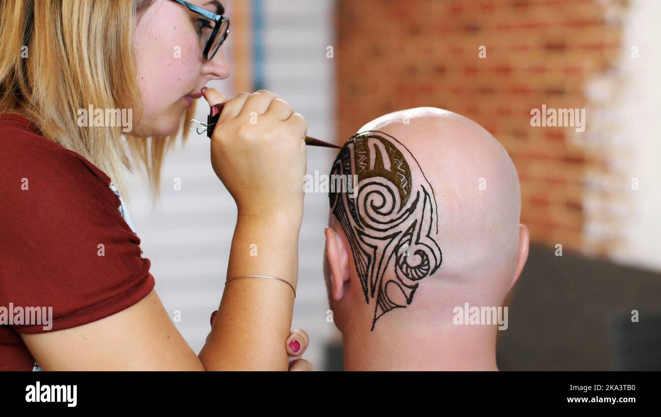 A close-up, the execution of a master, an artist mehendi, a tattoo, a picture of henna on white skin scalp, a bald Caucasian man. Black, dark brown abstract ornaments. High quality photo Stock Photo
