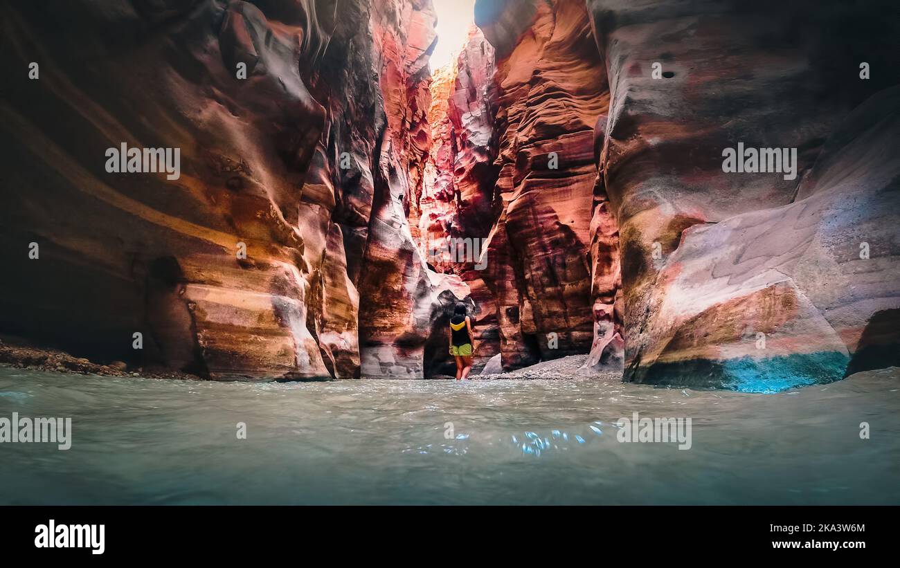 Female tourist walk in water in famous river canyon of Wadi Mujib in amazing golden light colors. Wadi Mujib travel destination in Jordan Stock Photo