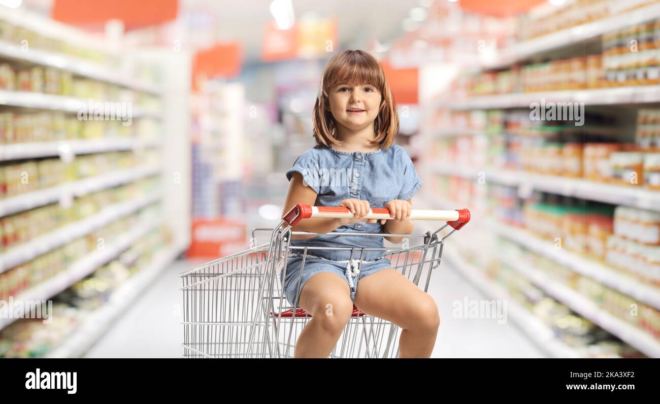 Child sitting in a shopping cart inside a supermarket and looking at