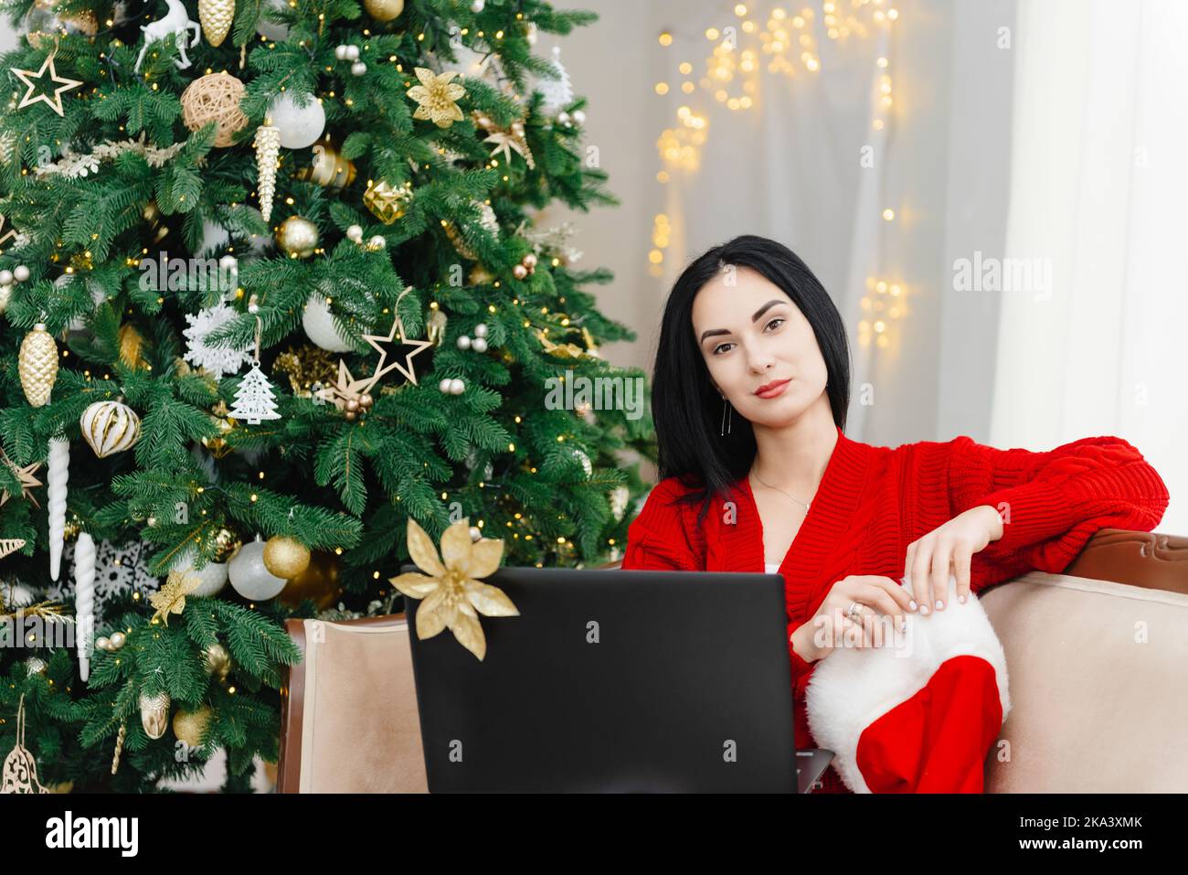 A girl in a red knit sweater with a laptop, sitting and looking straight into the camera. site search, discounts on winter shopping, text, sitting Stock Photo