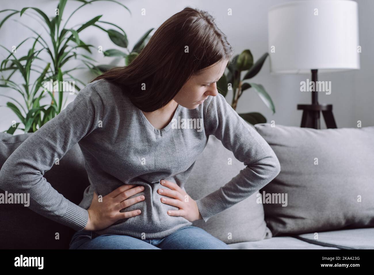 Sick young woman in pain holding belly stomach feeling hurt abdomen