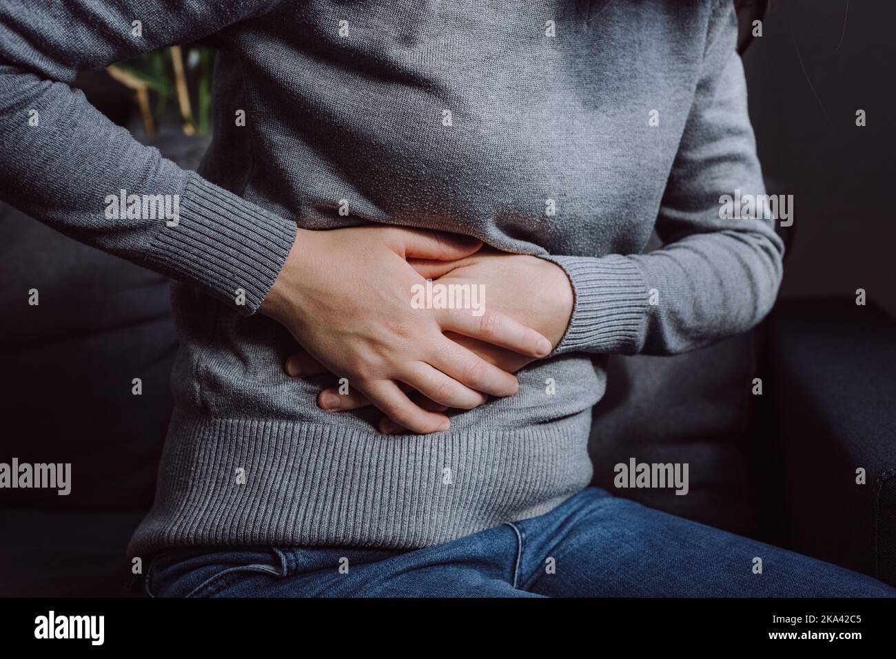 Flatulence young woman sitting on couch at home. Unhealthy girl suffer from food poisoning, abdominal pain and colon problem, gastritis or diarrhoea. Stock Photo