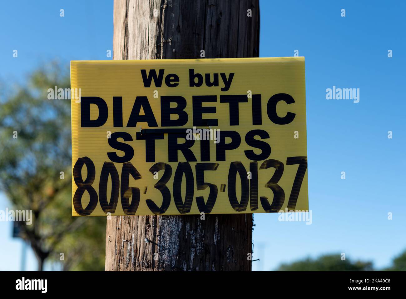 A bright yellow sign attached to a power pole reads We Buy Diabetic Strips. Stock Photo