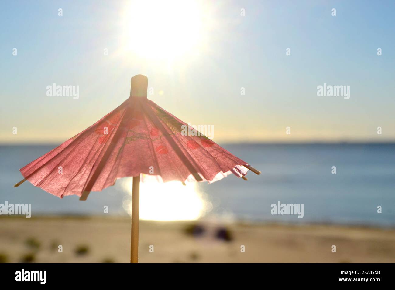 One red paper umbrellas cocktail decorations on background of blue sky, brightly shining sun and sunny path on surface of blue sea. Concept of summer, sea, vacation, travel tourism Stock Photo