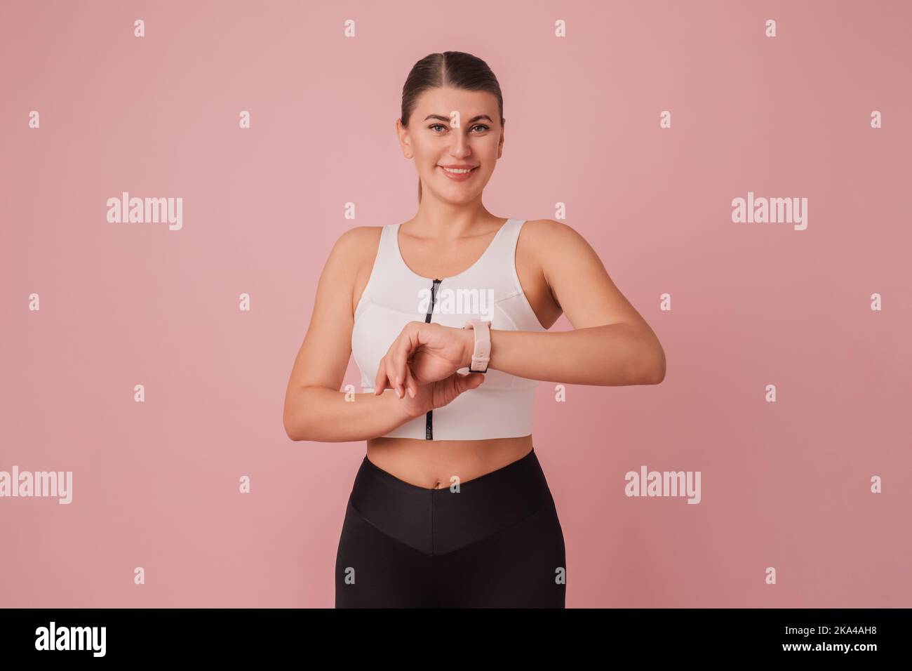 Time to fitness. Sport motivation concept. Young woman in sportswear with fitness watch on pink background Stock Photo