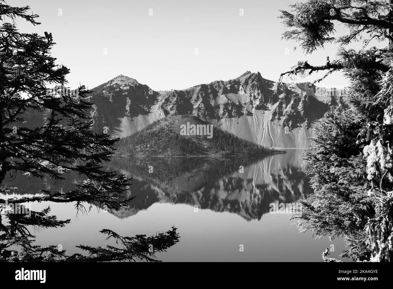 Black and white image of the Wizard Tower in Crater Lake, Oregon. The crystal clear water creates a mirror reflection of the island and the surrounding. Stock Photo