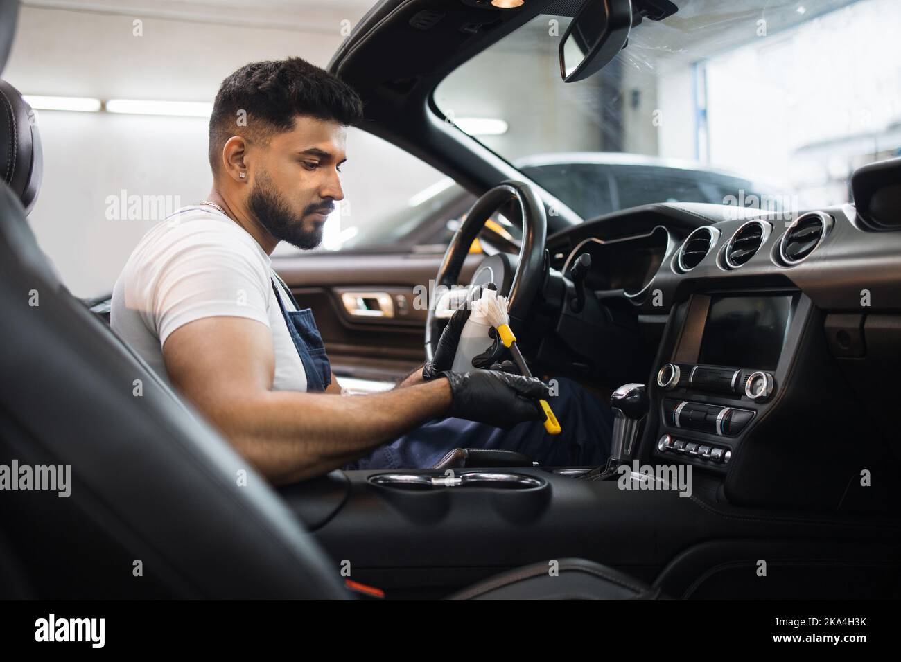 Bearded young male car detailing worker in overalls, sitting inside of