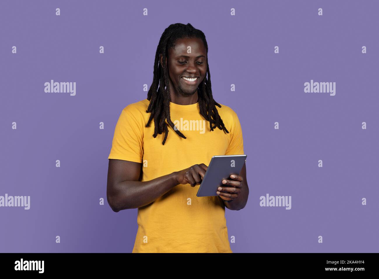 Happy stylish black guy using digital tablet on purple Stock Photo