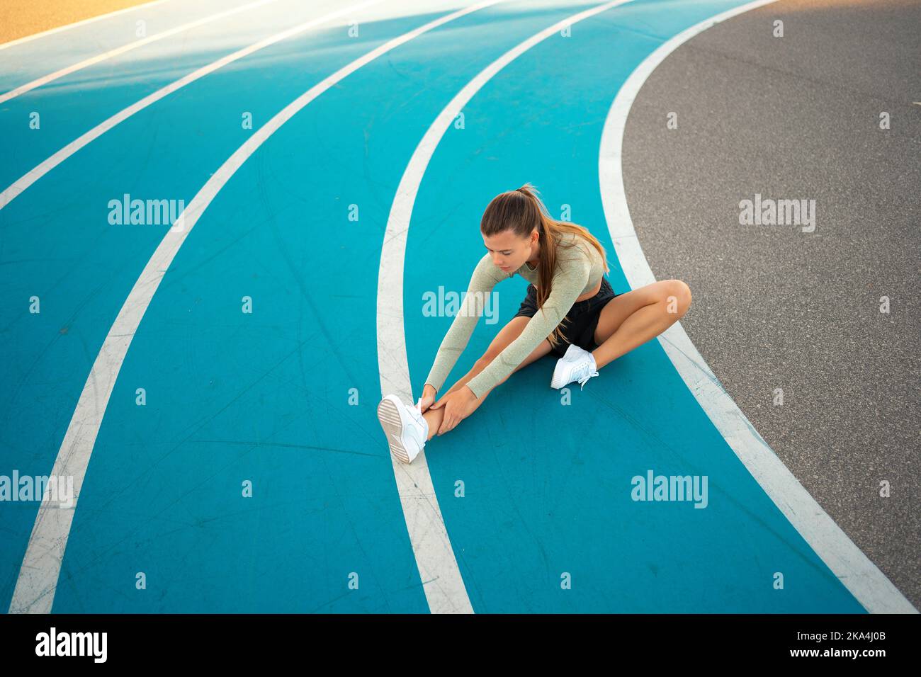 Sportswoman sitting and stretching on blue track field. Woman runner