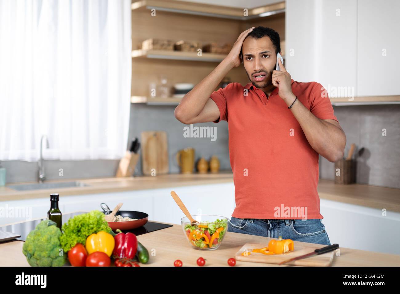 Sad confused young african american guy in red tshirt holds his head