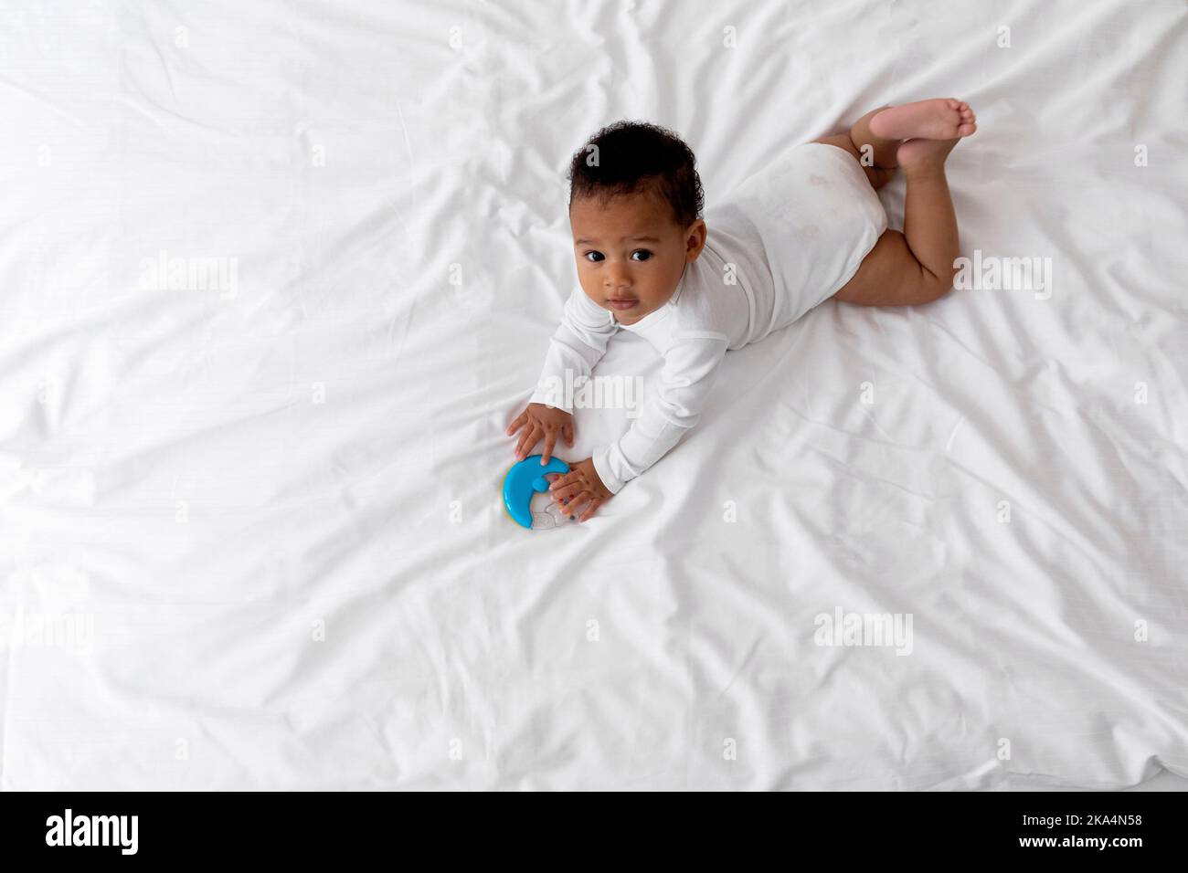 Cute Black Baby Playing With Rattle Toy While Lying On Bed Stock Photo