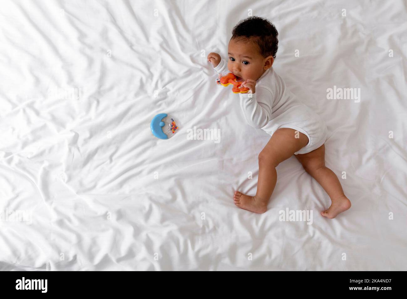 Adorable African American Infant Baby Lying In Bed And Biting Teether