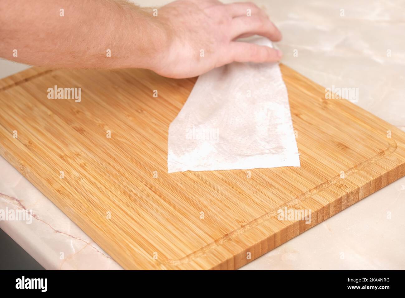 A man wipes a bamboo cutting board with a white paper napkin after