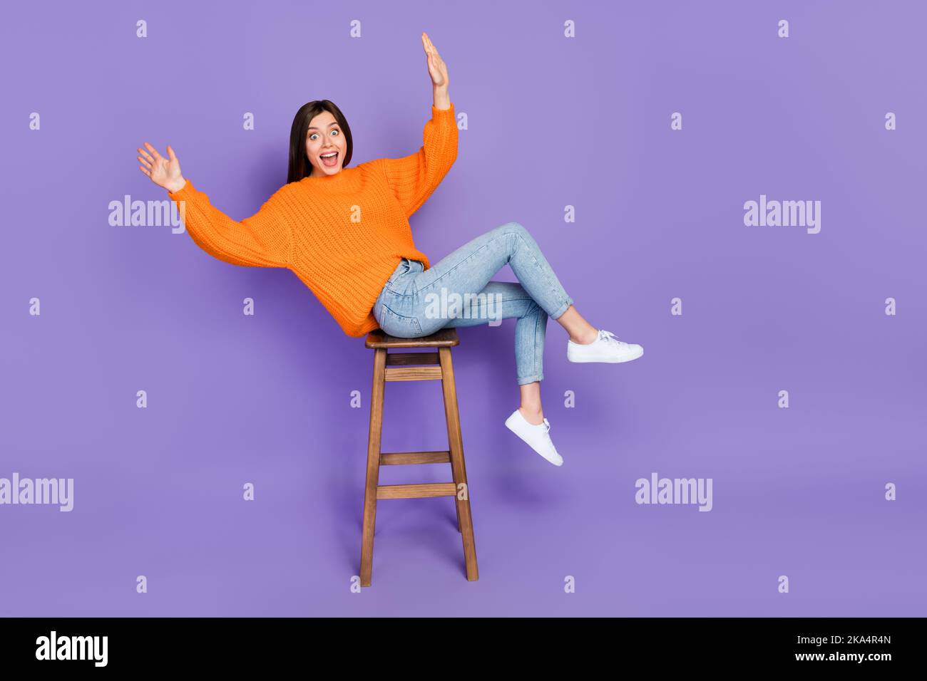 Full size photo of lovely young woman sit stool falling lean over dressed stylish orange knitted outfit isolated on purple color background Stock Photo