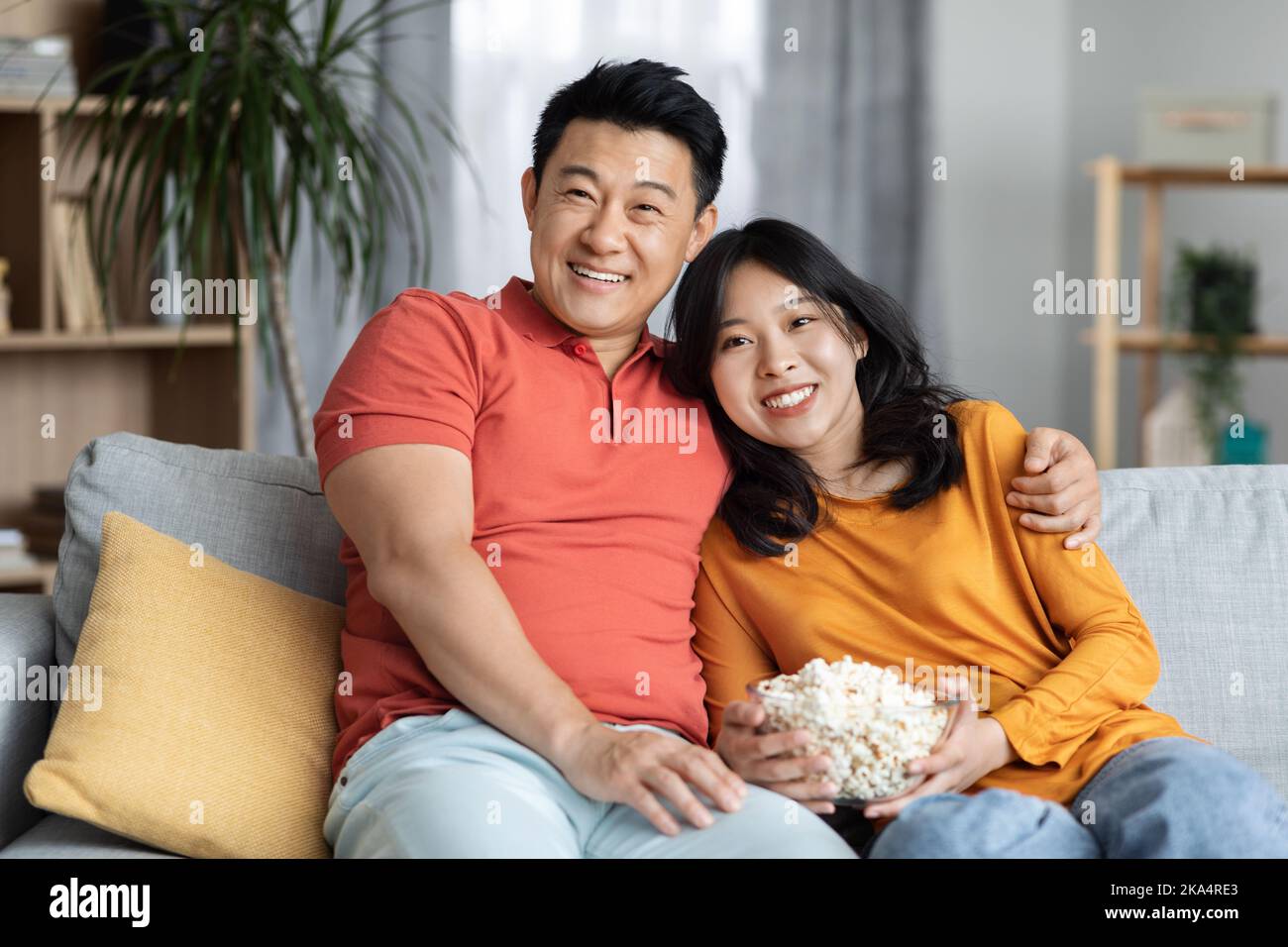 Relaxed korean spouses sitting on sofa, watching movie together Stock Photo