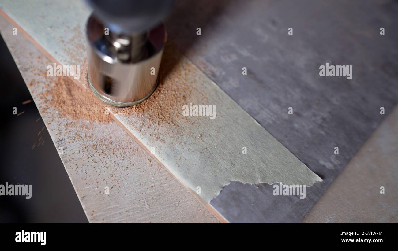 A worker drills a hole in a ceramic tile. A tiler is using a diamond